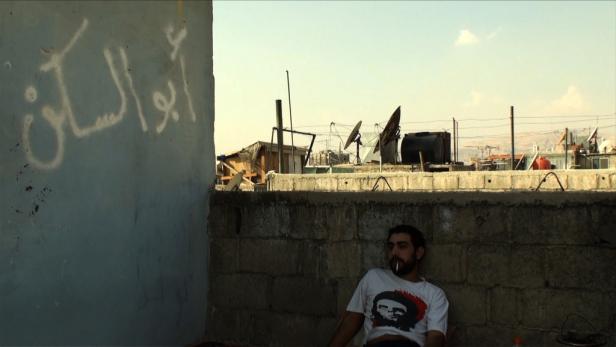 Ein Mann mit Che-Guevara-T-Shirt raucht auf einer Dachterrasse mit arabischer Graffiti im Hintergrund.
