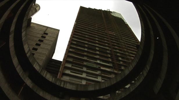 Ein unfertiges Hochhaus wird durch die konzentrischen Kreise einer Betonstruktur hindurch betrachtet.