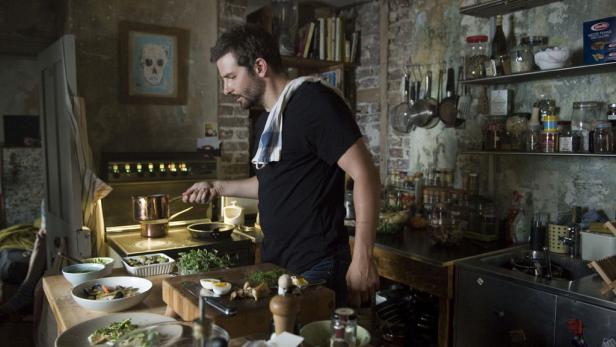 Ein Mann kocht in einer rustikalen Küche mit Zutaten auf dem Tisch.