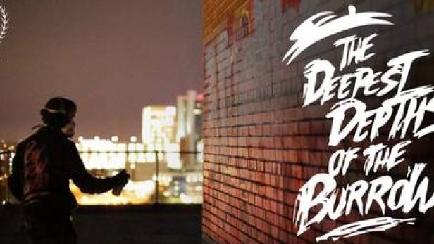 Eine Person sprüht den Titel „The Deepest Depths of the Burrow“ auf eine Ziegelmauer.