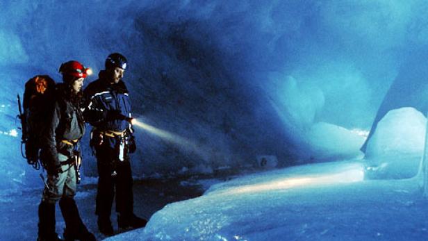 Zwei Personen erkunden eine Eishöhle mit Stirnlampen und einer Taschenlampe.