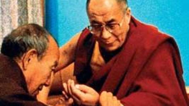 Der Dalai Lama betrachtet etwas in den Händen eines anderen Mannes.