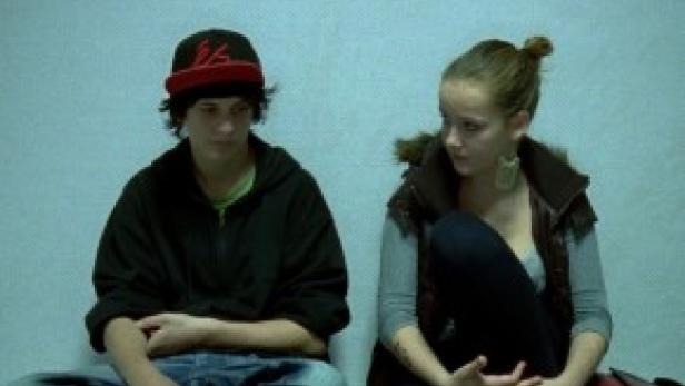 Zwei junge Menschen sitzen nebeneinander auf dem Boden.