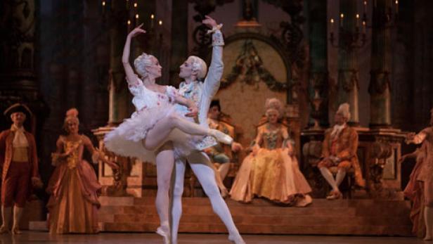 Ein Ballettpaar tanzt auf einer Bühne vor einem opulenten Bühnenbild.
