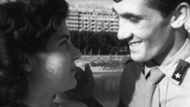 Ein junger Soldat und eine junge Frau stehen einander gegenüber und lächeln sich an.