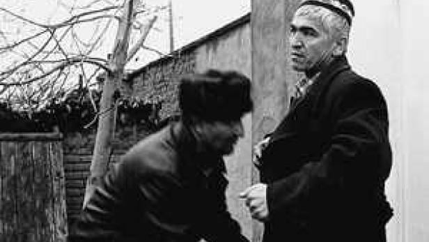 Zwei Männer stehen im Freien, einer mit traditioneller Kopfbedeckung.