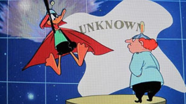 Daffy Duck als Weltraumheld hängt von der Decke, während ein Wissenschaftler zusieht.