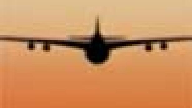 Die Silhouette eines Flugzeugs vor einem orangefarbenen Himmel.