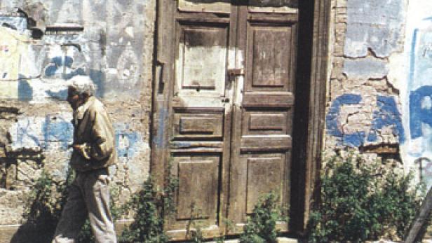 Ein älterer Mann geht an einer verfallenen Tür vorbei.