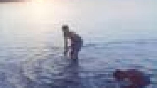 Zwei Personen stehen im flachen Wasser, möglicherweise bei Sonnenaufgang oder -untergang.