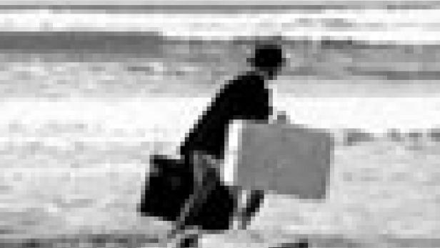 Ein Mann mit Anzug und Hut rennt mit Koffern am Strand entlang.