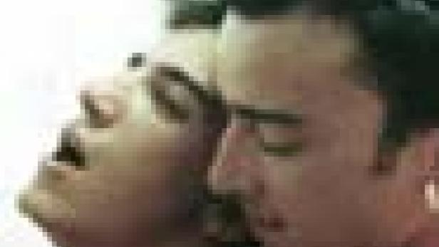 Ein Mann und eine Frau stehen eng beieinander, die Frau mit geöffnetem Mund und zurückgelehntem Kopf.