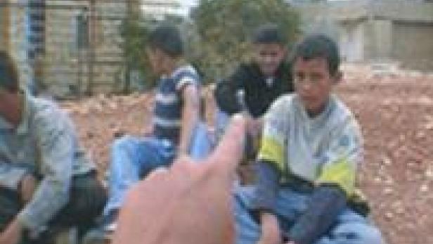 Eine Gruppe von Jungen sitzt auf dem Boden, während ein Finger auf einen von ihnen zeigt.