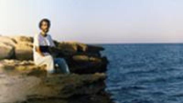 Ein Mann sitzt auf einer Klippe mit Blick auf das Meer.