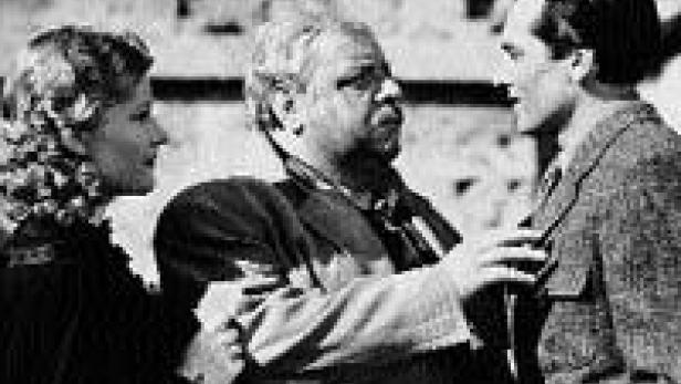 Drei Personen, eine Frau und zwei Männer, stehen in einer Schwarzweißaufnahme zusammen.