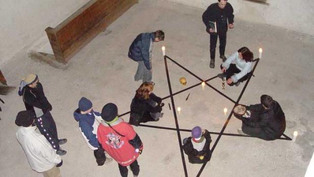 Eine Gruppe von Menschen steht um einen Pentagramm-Altar mit Kerzen und einem Schädel.
