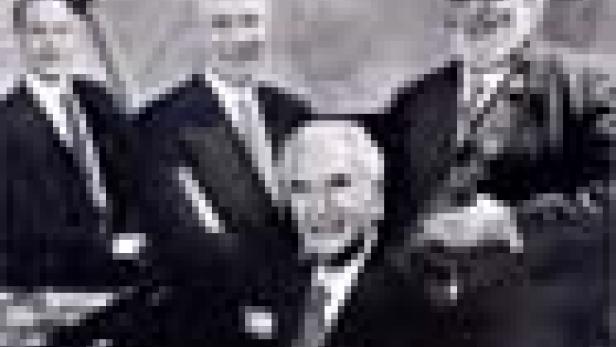 Eine Schwarzweißaufnahme von vier älteren Herren in Anzügen, die ein Streichquartett bilden.