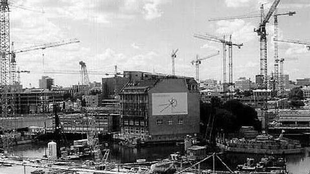 Zahlreiche Baukräne prägen die Skyline einer Stadt am Wasser.