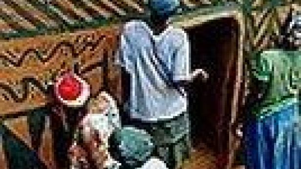 Eine Gruppe von Menschen steht vor einem traditionellen afrikanischen Haus.