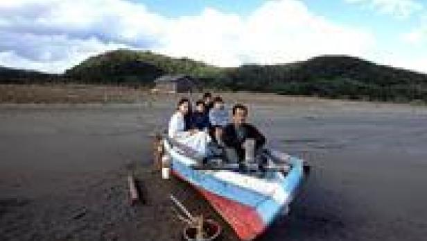 Eine Gruppe von Menschen sitzt in einem bunten Boot am Strand.