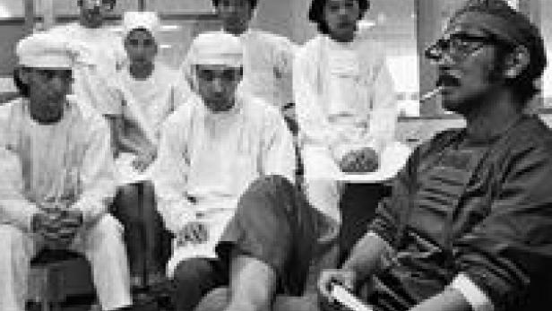 Eine Gruppe von Männern, einige mit Kopfbedeckung, sitzt oder steht in einem Raum.