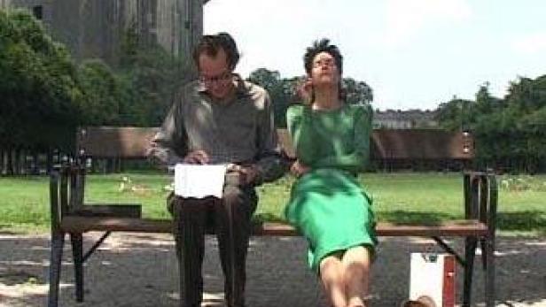 Ein Mann und eine Frau sitzen auf einer Parkbank; die Frau genießt die Sonne.