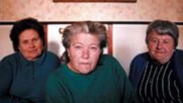 Drei ältere Frauen sitzen nebeneinander vor einer Wand mit einem Bild.