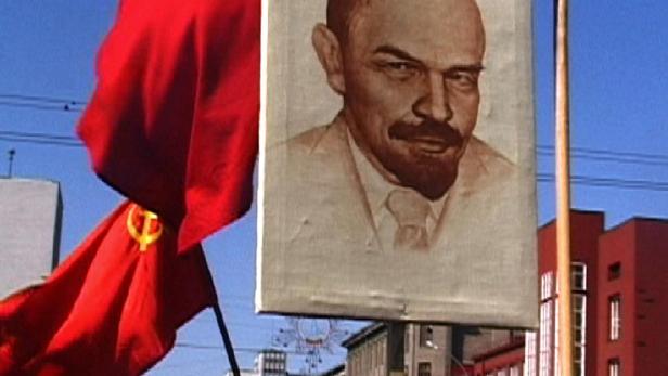 Eine rote Flagge mit Hammer und Sichel und ein Porträt von Lenin bei einer Demonstration.