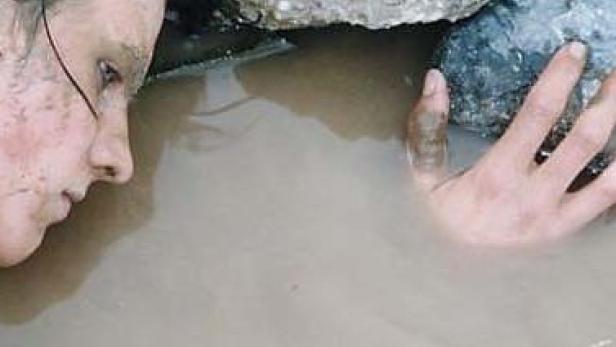 Eine Frau liegt mit schmutzigem Gesicht in trübem Wasser.