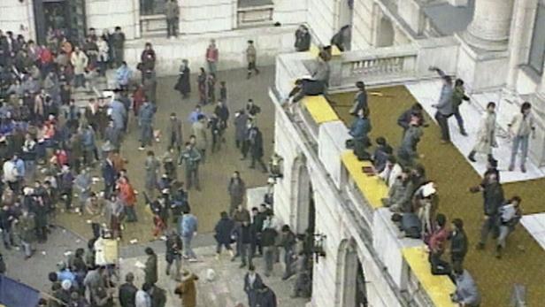 Eine Menschenmenge versammelt sich vor einem Gebäude, einige auf dem Dach, möglicherweise während einer Demonstration.