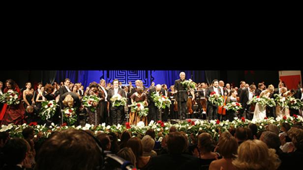 Ein Orchester und Sänger nehmen auf einer Bühne den Applaus des Publikums entgegen.
