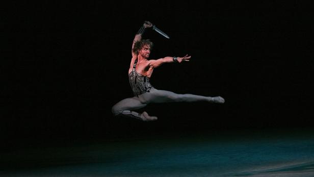 Ein männlicher Ballettänzer springt mit einem Dolch in der Hand auf der Bühne.