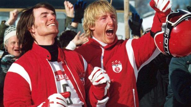 Zwei jubelnde kanadische Skirennläufer in roter Teamkleidung mit einem roten Skihelm.