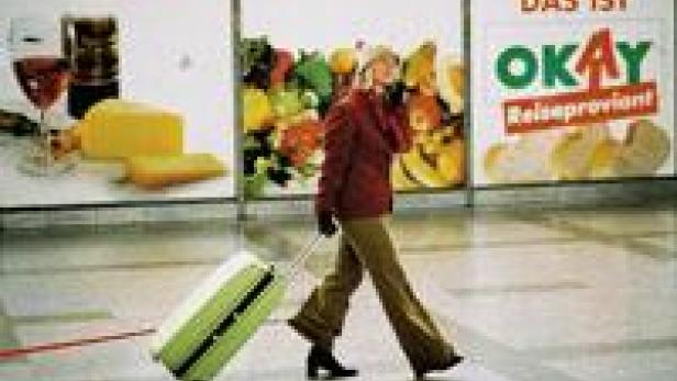 Eine Frau zieht einen Rollkoffer vor Werbeplakaten her.