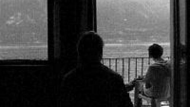 Zwei Personen sitzen auf einem Balkon mit Blick auf einen See.