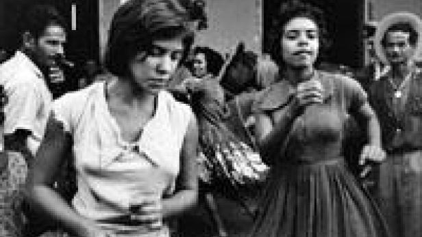 Schwarzweißaufnahme von zwei jungen Frauen, die tanzen, umgeben von weiteren Personen im Hintergrund.