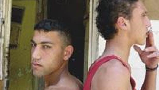 Zwei junge Männer stehen Rücken an Rücken, einer raucht eine Zigarette.