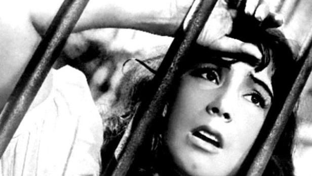 Eine verängstigte Frau blickt hinter Gittern hervor.