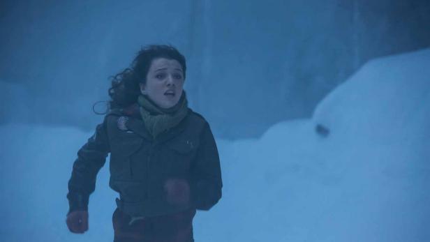 Eine Frau rennt in einer verschneiten Landschaft mit besorgtem Gesichtsausdruck.