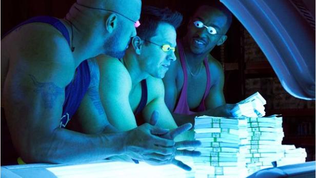 Drei Männer mit Schutzbrillen stehen neben Stapeln von Banknoten.