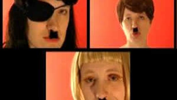 Drei Personen mit aufgemalten Hitler-Bärten vor einem roten Hintergrund.