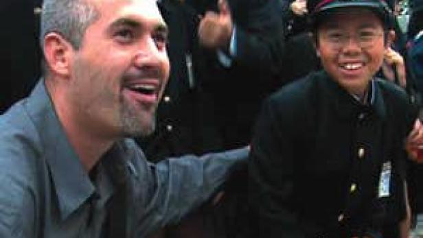 Ein Mann lächelt neben einem Jungen in Schuluniform.