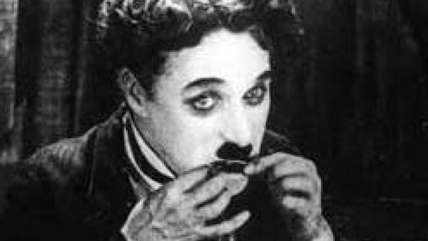 Ein Schwarzweißporträt von Charlie Chaplin, der seinen ikonischen Schnurrbart richtet.