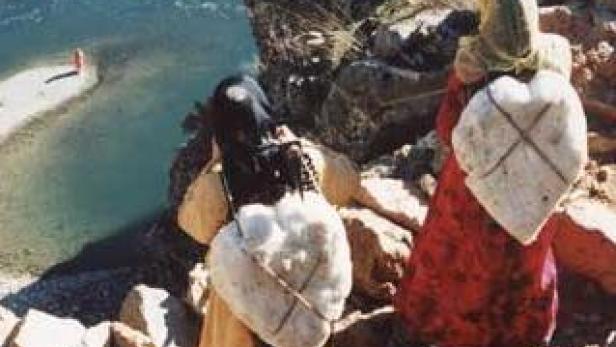 Zwei Frauen tragen Wasser in Behältern am Flussufer.