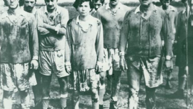 Eine Gruppe schlammbedeckter Fußballspieler steht auf einem Feld.