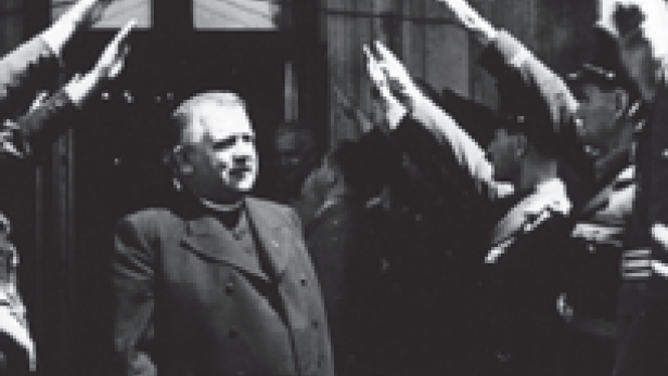 Ein Mann in Zivilkleidung wird von uniformierten Männern mit erhobenem Arm gegrüsst.