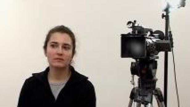 Eine Frau sitzt vor einer Kamera und einem Scheinwerfer.