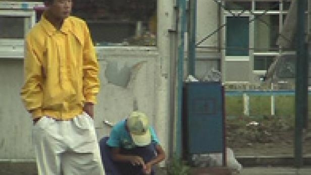 Zwei junge Männer warten an einer Bushaltestelle.