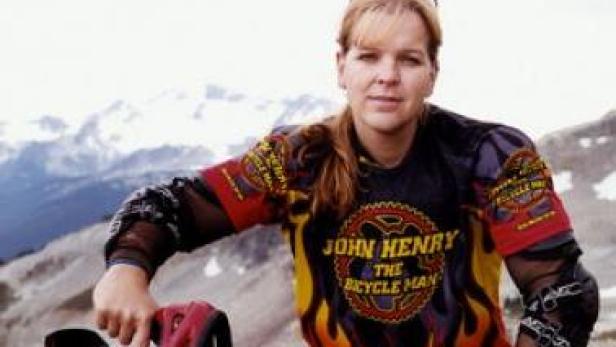 Eine Frau in Sportkleidung posiert vor einer Bergkulisse.