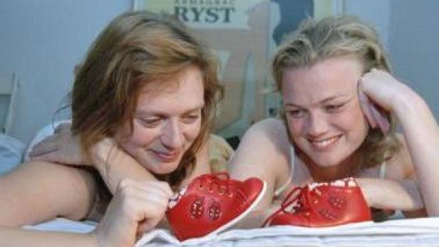 Zwei Frauen betrachten lächelnd rote Babyschuhe auf einem Bett.